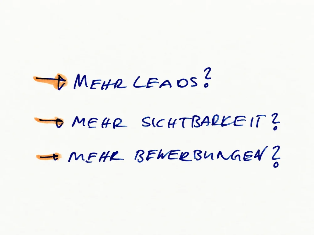 Handschriftliche Notiz mit drei Zielen, jeweils mit Pfeil markiert: mehr Leads, mehr Sichtbarkeit, mehr Bewerbungen.